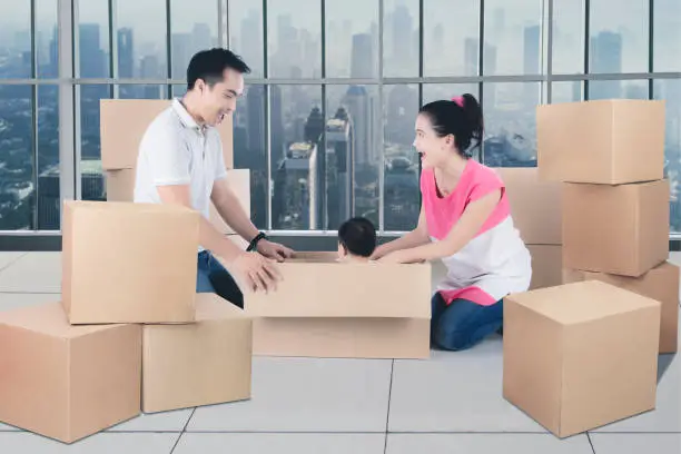 Young Asian family having fun unpacking boxes moving in to a new apartment