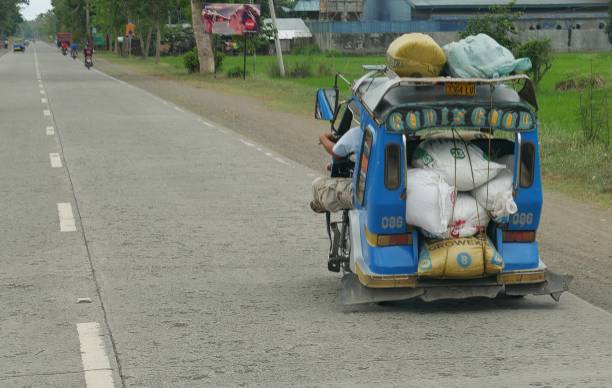 blue tricycle, or motorcycle with sidecar DAVAO  DEL NORTE, PHILIPPINES—A blue tricycle, or motorcycle with sidecar overloaded with various cargo at the national highway in Mabini, Davao del Norte, southern Philippines in March 2016. philippines tricycle stock pictures, royalty-free photos & images