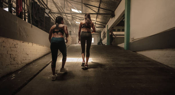 Two women walking in the cross training gym. Shot from behind of fitness females going in the health club.