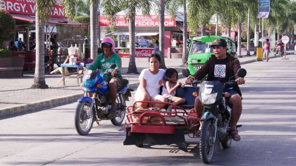 Passengers riding a motorcycle with a sidecar, TAGUM CITY, PHILIPPINES—FEBRUARY 2016: Passengers riding a motorcycle with a sidecar, called trisikad which is a popular public transportation in the Philippines. philippines tricycle stock pictures, royalty-free photos & images