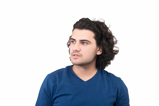Portrait of young man looking away with blank facial expression by standing over white background. Horizontal composition. Studio shot.