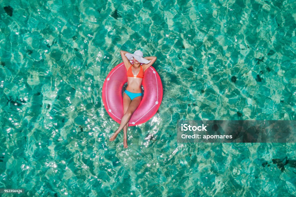 Aerial view of a young women relaxing on inflatable ring in a tropical turquoise pristine beach Aerial view of a young women relaxing on inflatable ring in a tropical turquoise pristine beach. Los Juanes, Morrocoy, Venezuela Inflatable Swim Ring Stock Photo