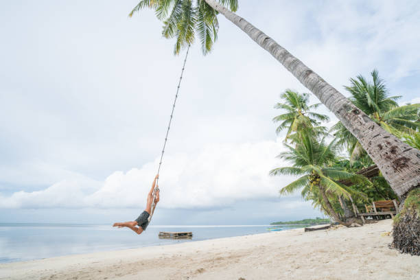 istock Young man paying on beach, swing rope on palm tree 952360456