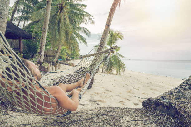 uomo felice che si rilassa sull'amaca sulla spiaggia tropicale sotto le palme - hammock beach vacations tropical climate foto e immagini stock