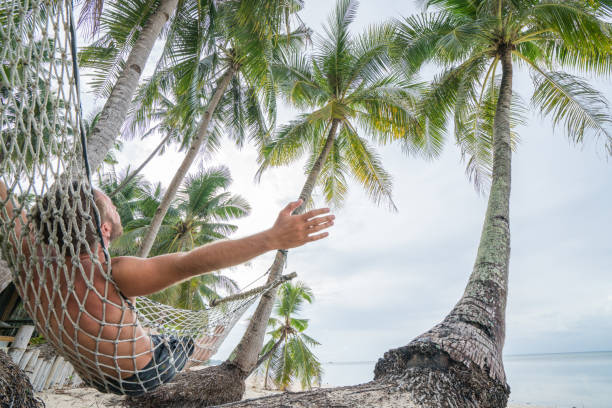 istock Happy man relaxing on hammock on tropical beach under palm trees 952360842