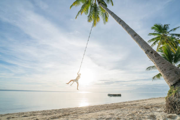 istock Young man playing on beach, swing rope on palm tree 952366070