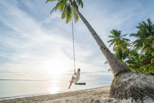 Young woman playing on beach, swing rope on palm tree