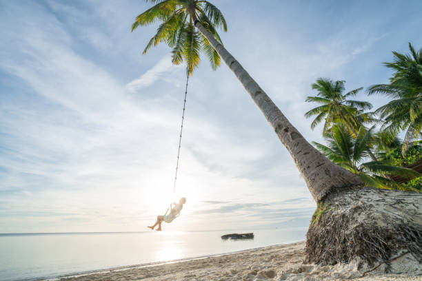 istock Young woman playing on beach, swing rope on palm tree 952366650