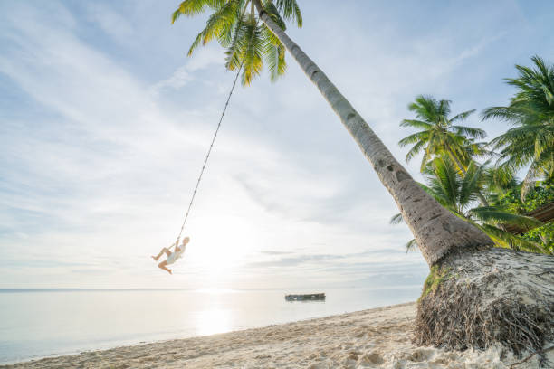 istock Girl playing on swing rope, tropical beach palm trees 952366672