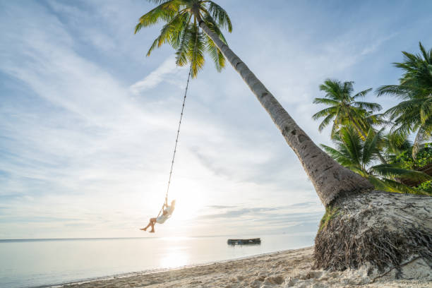 istock Young woman playing on beach, swing rope on palm tree 952366762