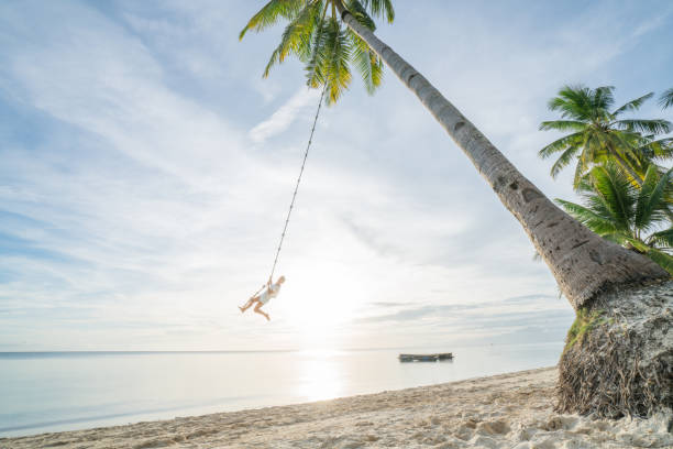 istock Girl playing on swing rope, tropical beach palm trees 952367000