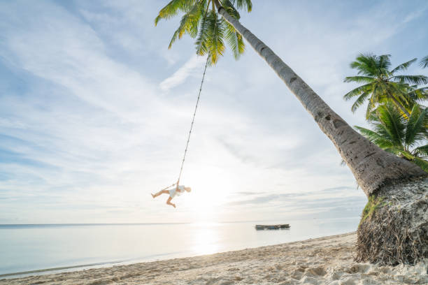istock Girl playing on swing rope, tropical beach palm trees 952367188