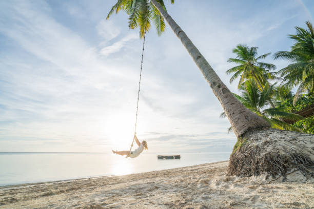istock Young woman playing on beach, swing rope on palm tree 952367194