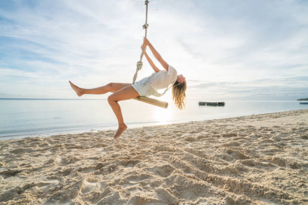 istock Girl playing on swing rope, tropical beach palm trees 952369682