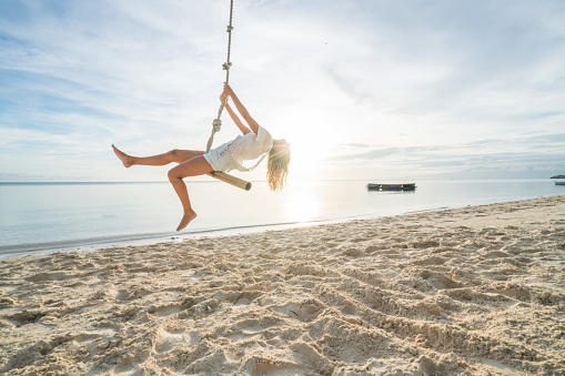 Young woman playing on beach, swing rope on palm tree. People travel exotic concept\nShot in the Philippines on tropical Island vacations
