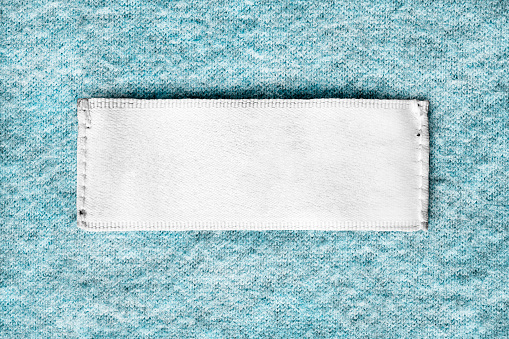 Blank white textile clothes label on blue cashmere background closeup