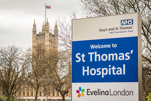 Exterior and signage of St Thomas Hospital with Houses of Parliament in backgound, a large NHS teaching hospital next to Westminster Bridge in central London