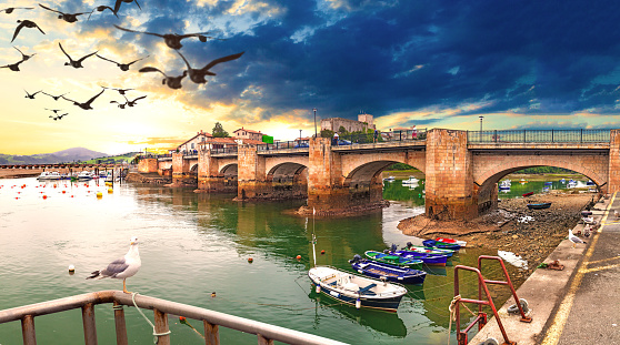 Idyllic and stunning coastal town in Spain. Bridge over the sea and sunset seascape. Boats in the harbor.