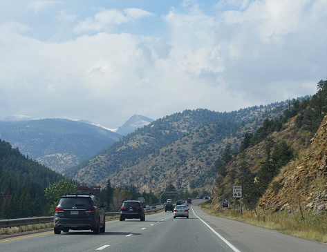 COLORADO, USA—OCTOBER 2017: Scenic view of winding road and cars running along Interstate 70 in the Colorado Rockies, with directional speed limit sign on the roadside.
