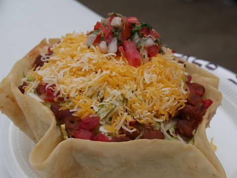 Close up of a taco loaded with hotdogs, salsa, jalapeno and topped with shredded cheese and sliced tomatoes.