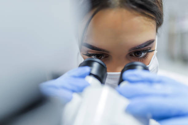 gros plan de jeune chercheur en regardant à travers un microscope dans un laboratoire - microscope laboratory scientist women photos et images de collection