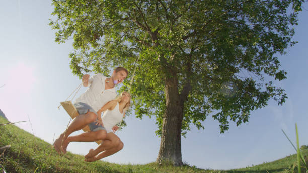 istock LOW ANGLE LENS FLARE: Young couple on swing illuminated by bright spring sunrays 952436910