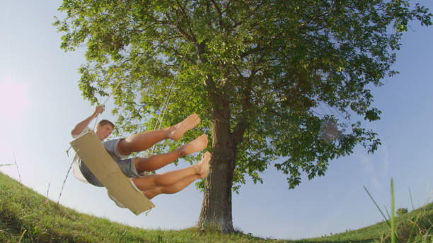 istock LOW ANGLE LENS FLARE Unrecognizable girlfriend and boyfriend swinging under tree 952436916