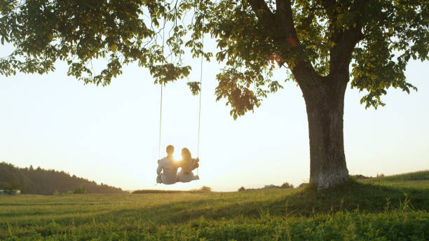 istock LENS FLARE SILHOUETTE: Setting sun shining over young couples shoulders on swing 952437150