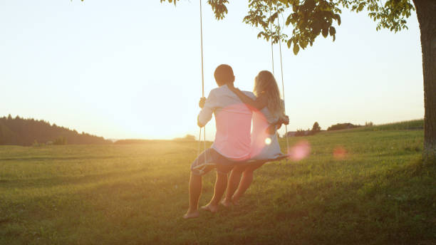 istock LENS FLARE: Romantic young couple watching sunset on swing on spring evening. 952437208