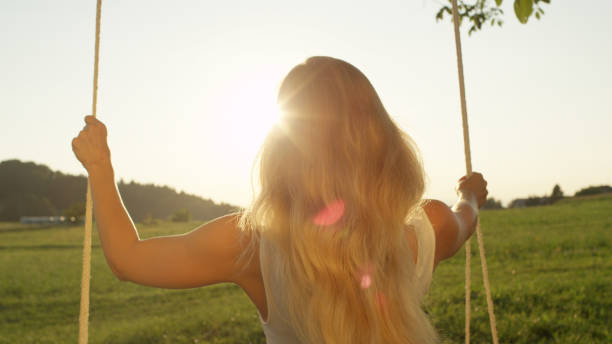 istock LENS FLARE, CLOSE UP: Unknown young blonde woman looking into sunset on swing. 952437332