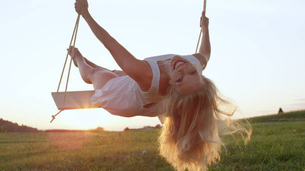 istock LENS FLARE CLOSE UP: Cheerful lady leaning back in her swing in golden nature. 952437364