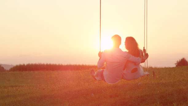 istock LENS FLARE: Happy couple swaying on a swing embraced on sunlit summer evening. 952437490