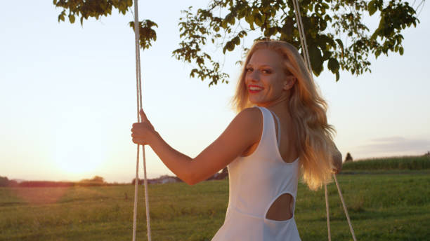 istock LENS FLARE, CLOSE UP: Cheerful lady turns around on her swing on sunny evening. 952437492