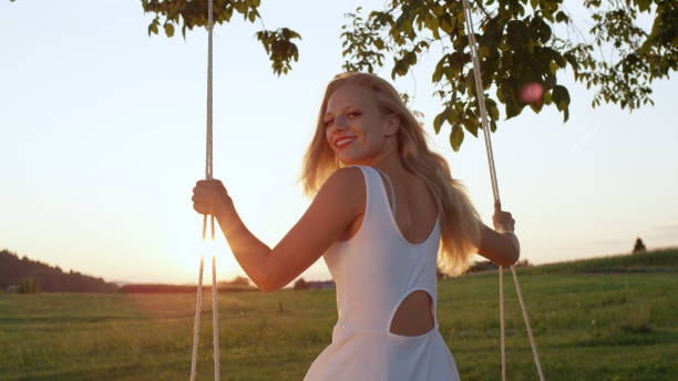 istock LENS FLARE, CLOSE UP: Joyful lady looking back on her swing on a sunny evening. 952437494