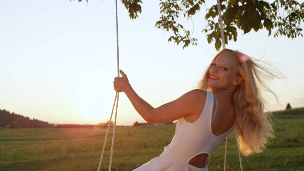 istock LENS FLARE CLOSE UP: Smiling young lady leaning back on her rope swing at sunset 952437500