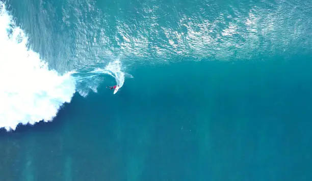 Photo of TOP DOWN: Unrecognizable pro surfer riding a stunning blue ocean wave in the sun