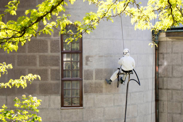A worker wearing a protective gear cleaning a stone facade Rope access facase maintenance; A worker wearing a protective gear cleaning a stone church exterior with abrasive blasting equipment hanging stone stock pictures, royalty-free photos & images