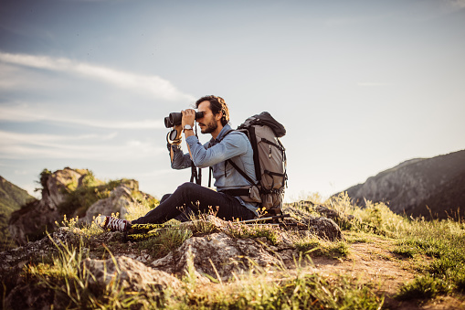 Young handsome hiker watching landscape with his binoculars