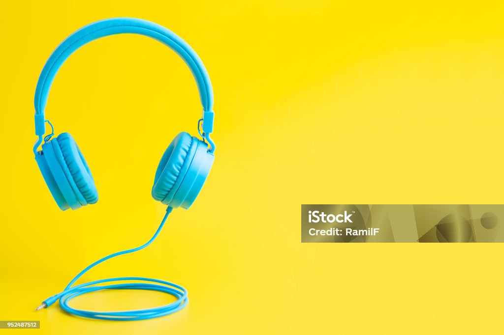 Bright blue headphones on yellow Minimalist bright composition of blue headphones on vibrant yellow background. Headphones Stock Photo
