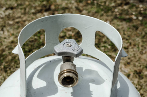 Angled overhead close-up of the top of a white propane tank and brass valve with grass in the background Angled overhead close-up of the top of a white propane tank and brass valve with grass in the background propane stock pictures, royalty-free photos & images