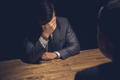 Suspect businessman displaying regret, worry and concern using body language in dark interrogation room
