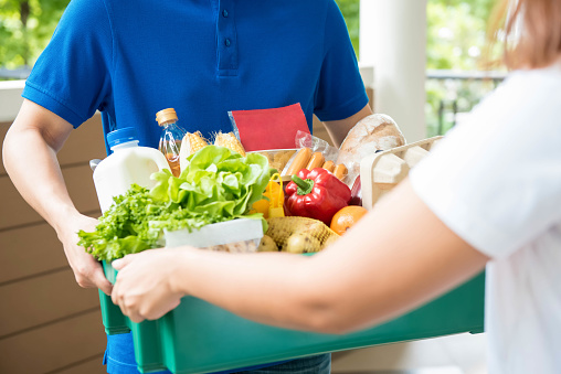 A grocery store delivery man wearing a blue polo-shirt delivering food to a woman at home