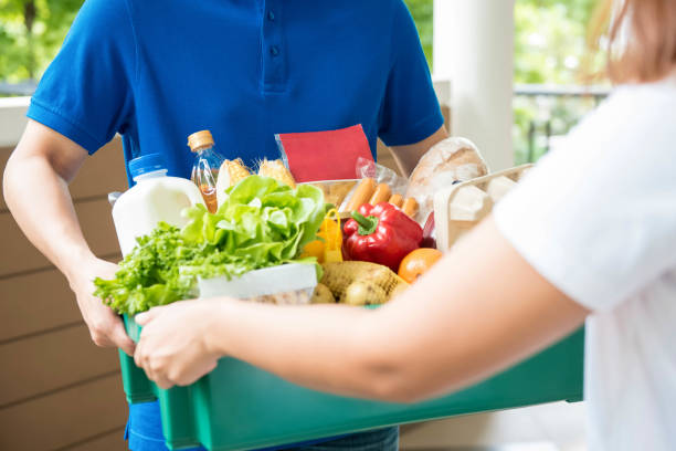 Agrocery delivery man delievering food to a woman at home A grocery store delivery man wearing a blue polo-shirt delivering food to a woman at home two men same clothes stock pictures, royalty-free photos & images