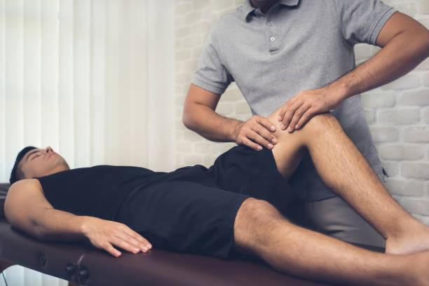 therapist treating injured leg of athlete male patient in clinic - deltoid imagens e fotografias de stock