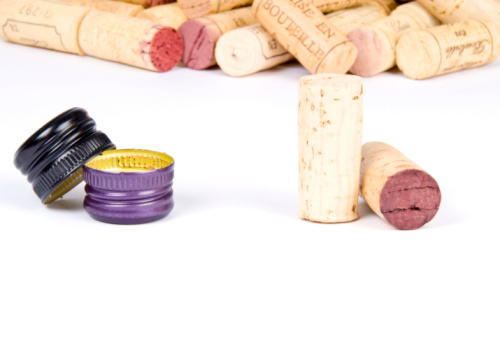 Bunch of corks in the background and two screw caps and two corks in the foreground in focus.