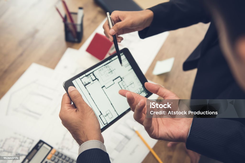 Real estate agent with client or architect team checking a housing model and its blueprints digitally using a tablet Real estate agent with client or architect team discussing a housing model and its blueprints digitally using a tablet computer Construction Industry Stock Photo