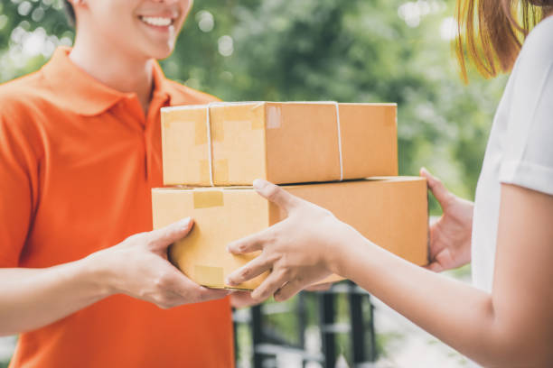 Smiling delivery man delivering parcel to a woman Smiling delivery man in orange uniform delivering parcel box to a woman customer - courier service concept door to door salesperson photos stock pictures, royalty-free photos & images