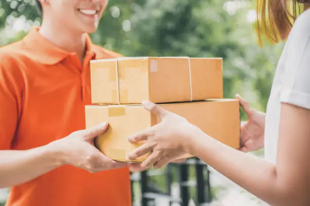 Smiling delivery man in orange uniform delivering parcel box to a woman customer - courier service concept