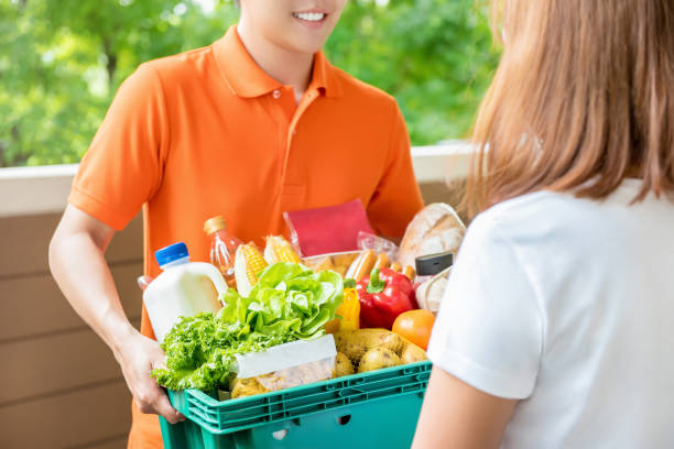 Grocery store delivery man delivering food to a woman at home Grocery store delivery man wearing an orange polo-shirt delivering food to a woman at home two men same clothes stock pictures, royalty-free photos & images