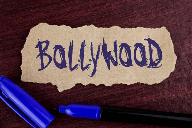 Photo of Handwriting text writing Bollywood. Concept meaning Indian cinema a source of entertainment written on Tear Cardboard paper piece on wooden background Marker next to it.